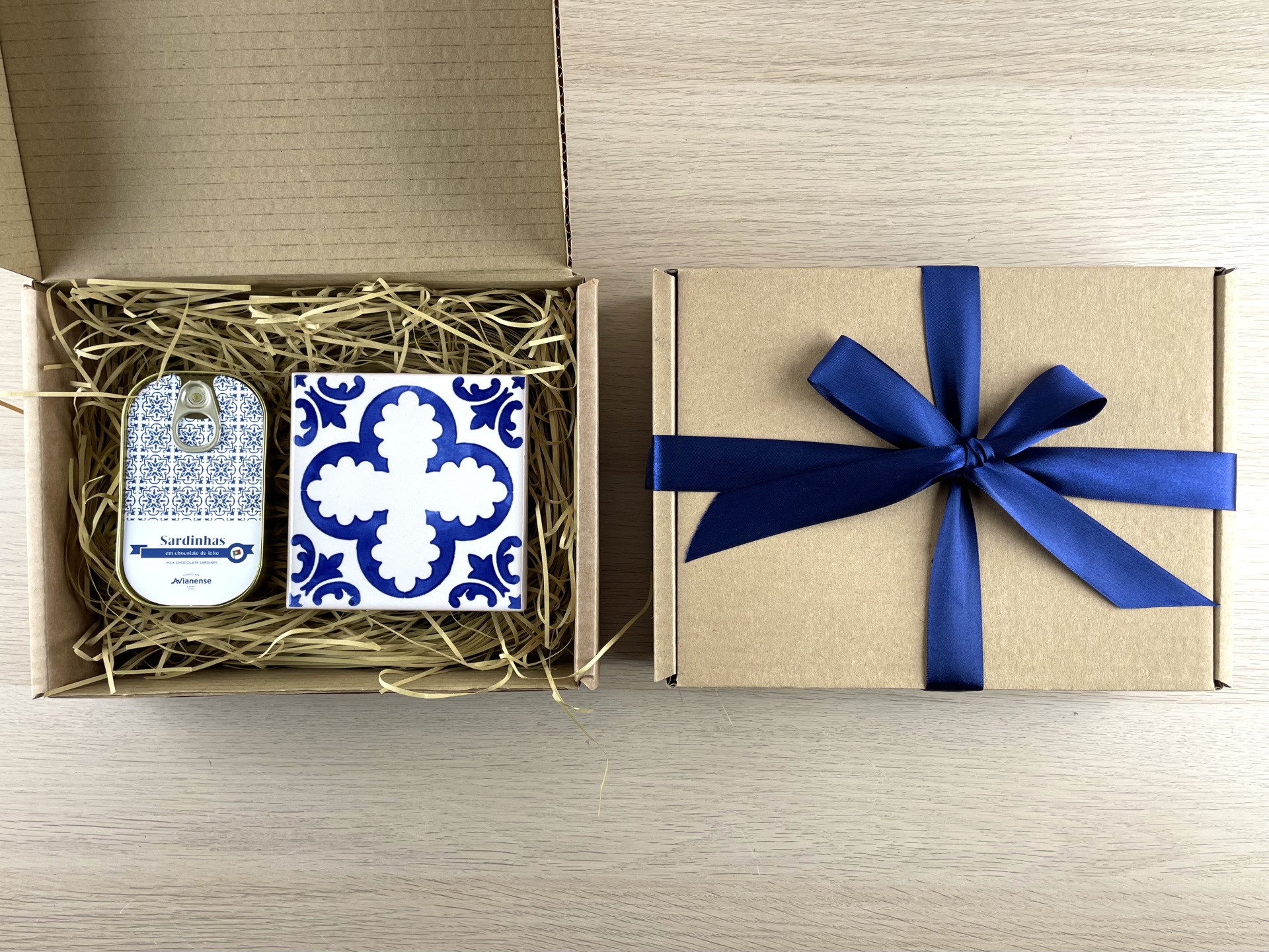 Gift set with a sardine tin and blue-white patterned ceramic tile in a kraft box with blue ribbon