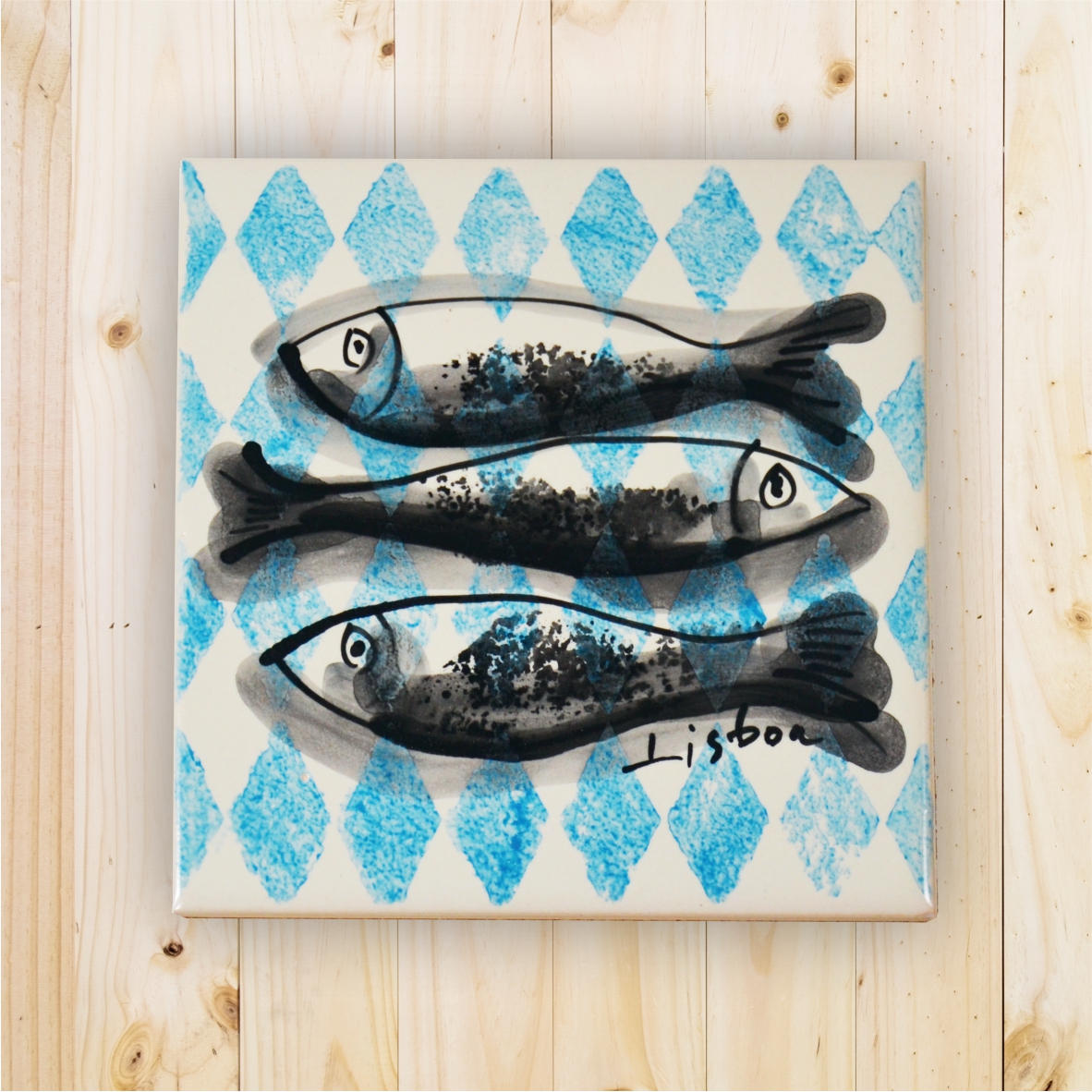 Ceramic tile with three black fish on blue diamond pattern and handwritten Lisboa text