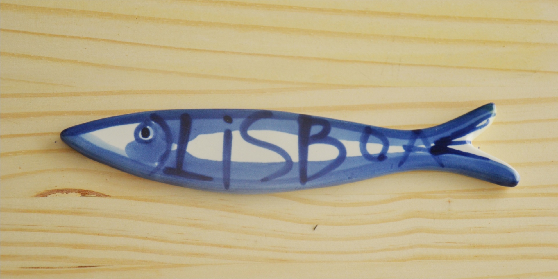 Blue and white ceramic fish ornament with LISBOA text on wooden surface