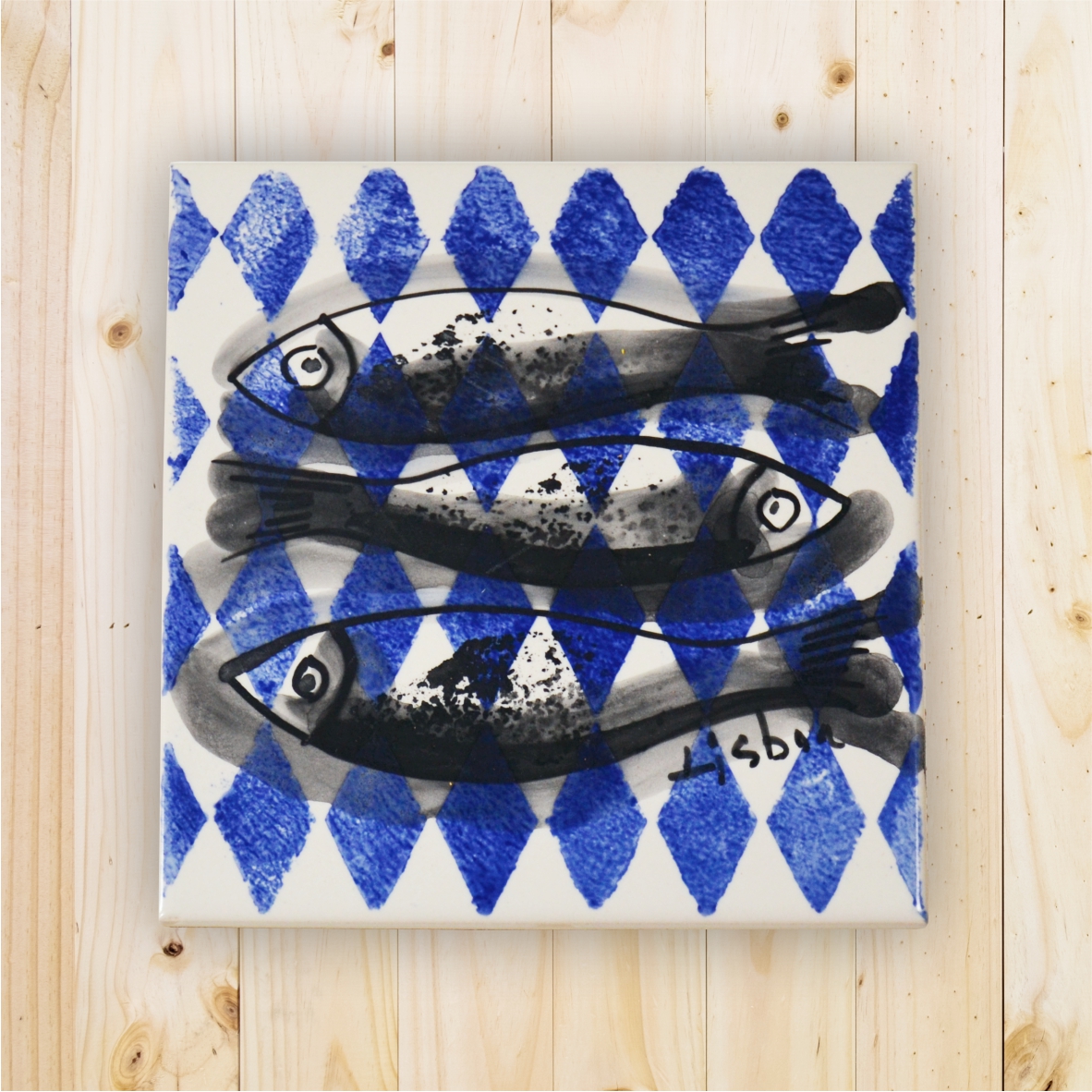Square ceramic tile with blue diamonds and three black fish illustration.