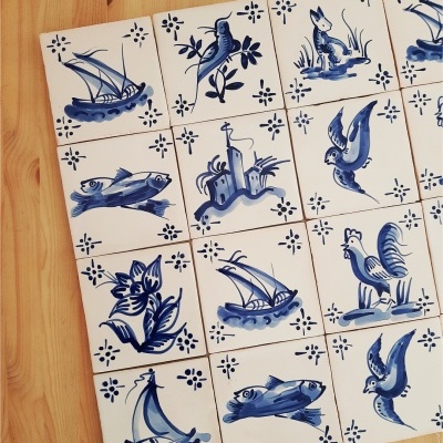Hand-painted blue and white ceramic tiles with various nature and nautical designs on wood