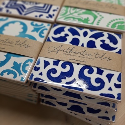 Stacks of ceramic tiles with intricate blue, green, turquoise patterns and Authentic tiles labels on wood.