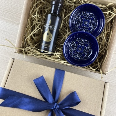 Gift box with bottle of olive oil and two blue ceramic saucers in straw packing.