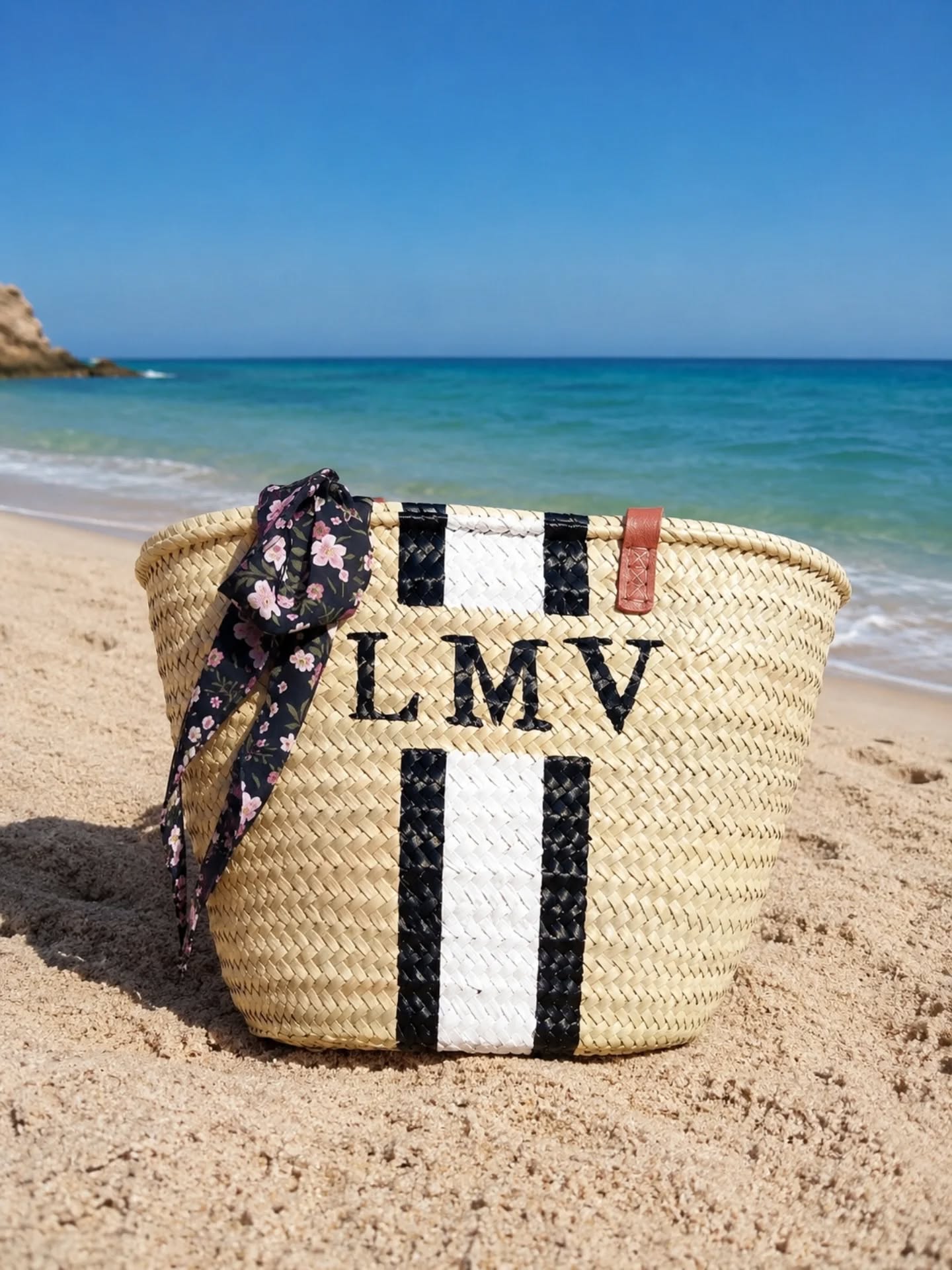Bolsa de praia em palha trançada com listras e texto LMV na areia da praia