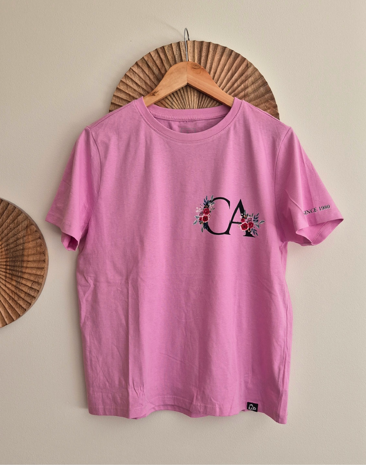 T-shirt rosa com logotipo e texto na manga pendurada num cabide