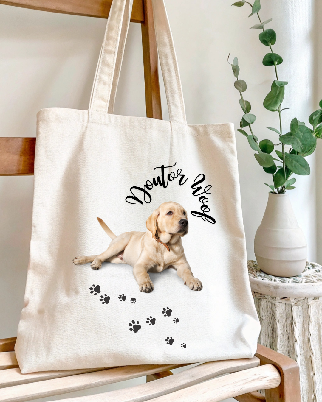 Saco de tecido cru com imagem de cão e texto 'Doutor Woof', pendurado em cadeira de madeira, com vaso branco e planta ao lado.