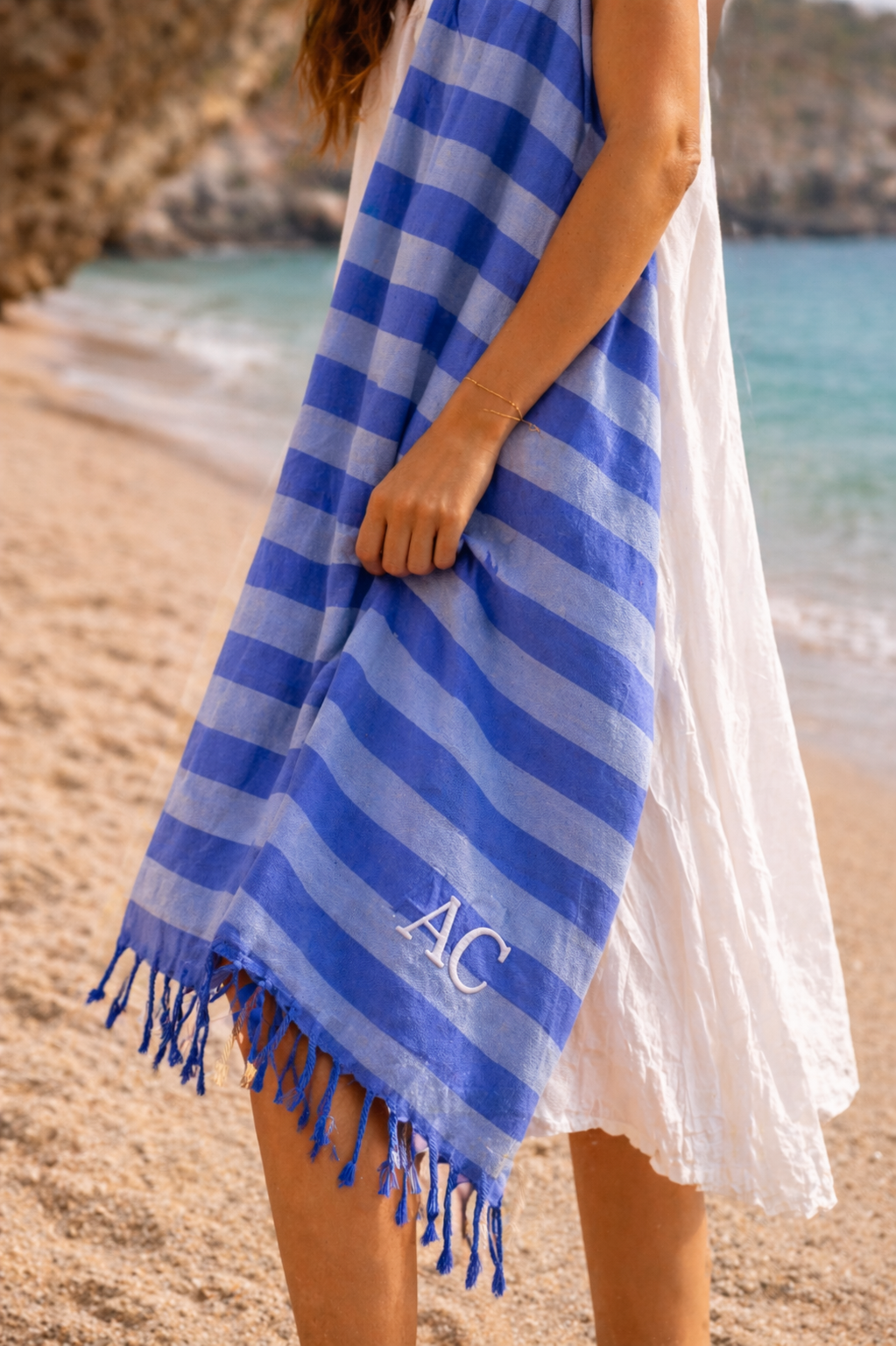 Toalha de praia azul com riscas e letras AC junto à praia.