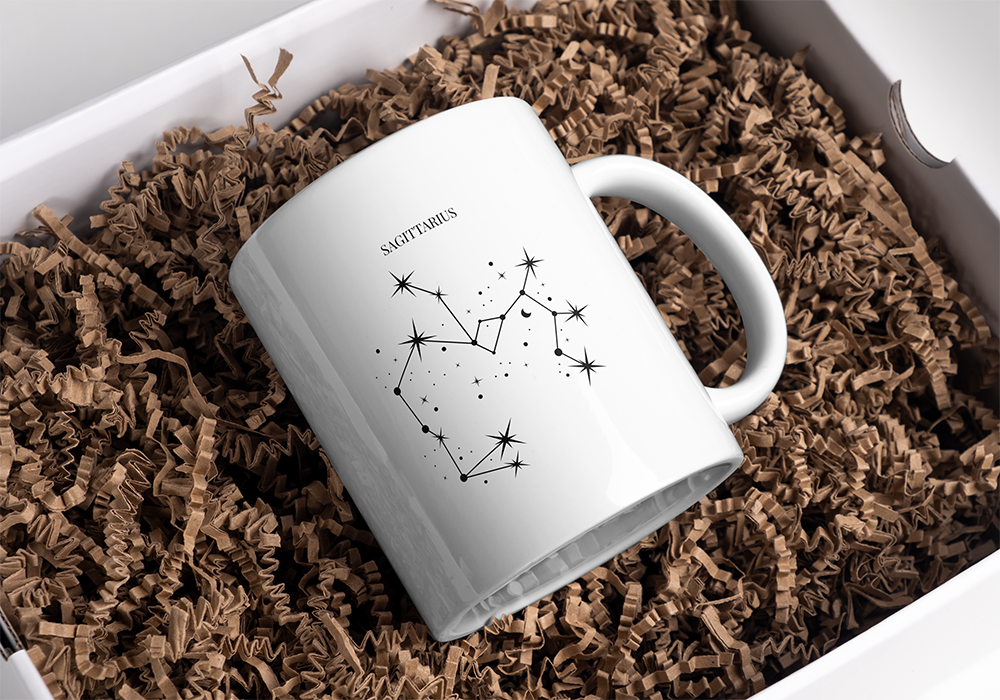 Caneca branca com constelação e texto S AGITTARIUS em caixa com papel castanho