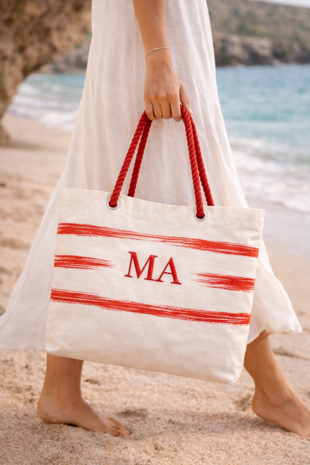 Saco de praia branco com riscas e alças vermelhas na mão de uma pessoa numa praia