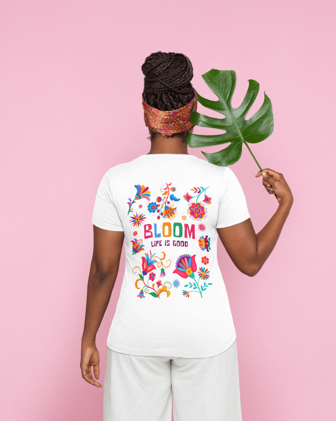 Pessoa vista de costas a usar t-shirt branca com estampa colorida floral e texto nas costas, segurando uma folha verde