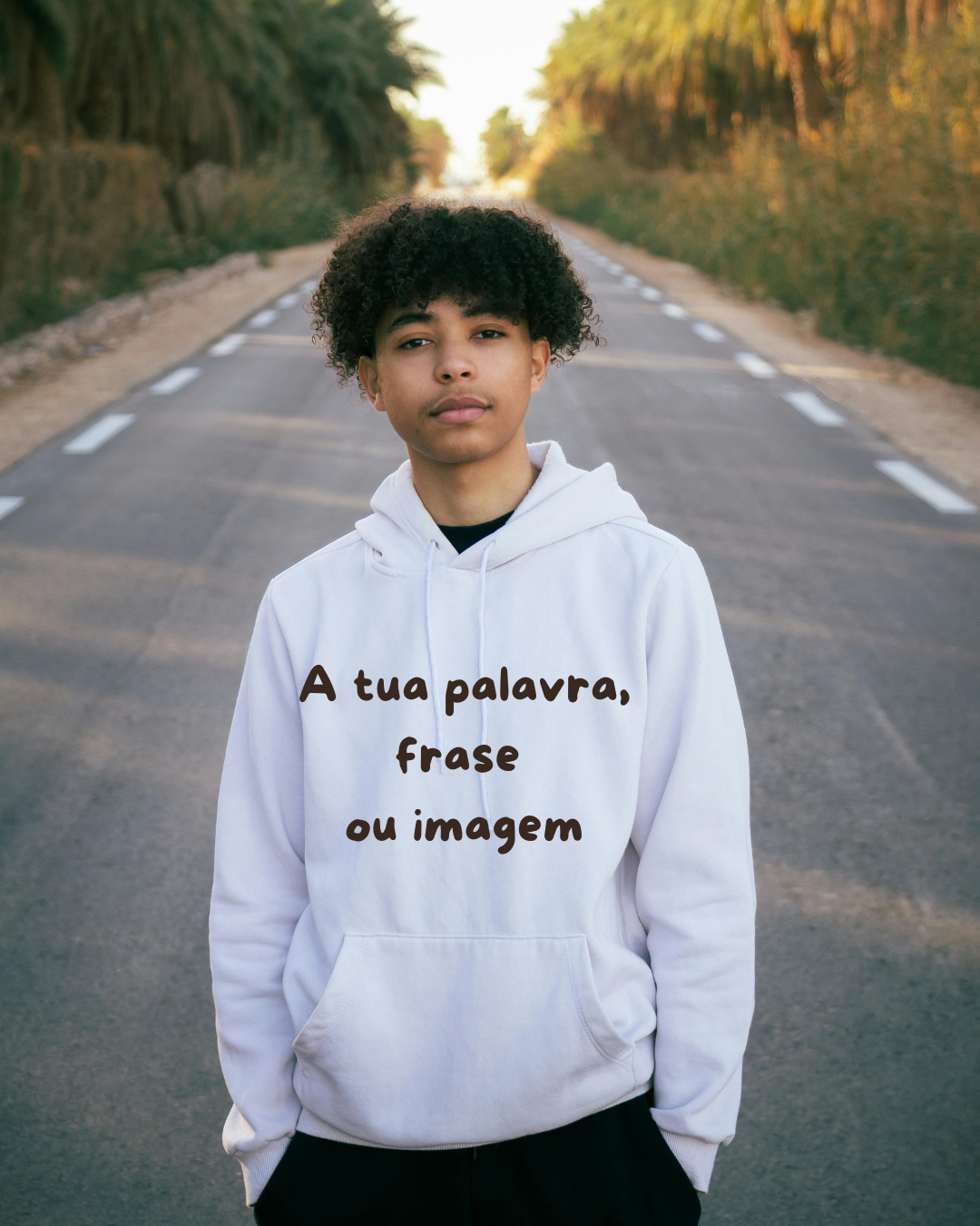 Jovem com sweatshirt branca com texto impresso, em estrada com árvores ao fundo
