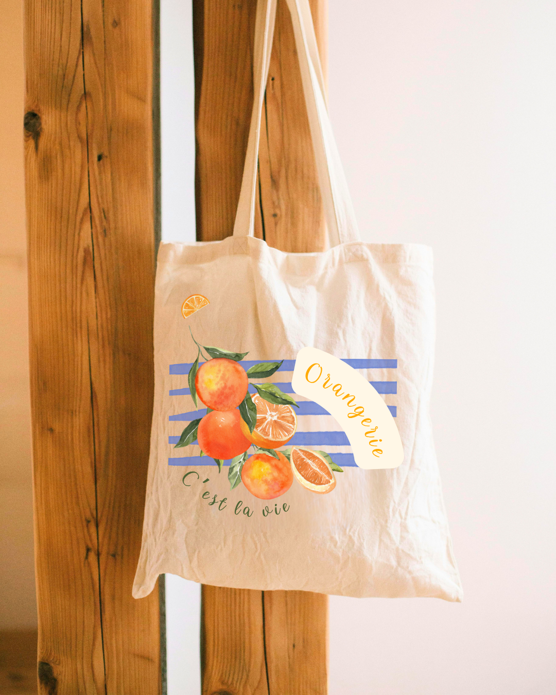 Saco de pano bege com estampado de laranjas e texto, pendurado em madeira