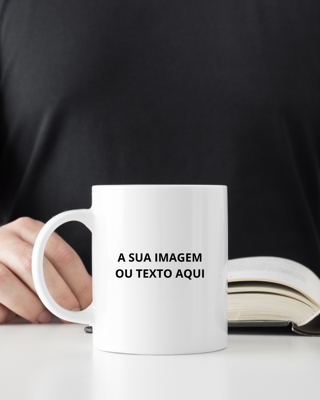Caneca branca com texto em preto segurada ao lado de livro aberto