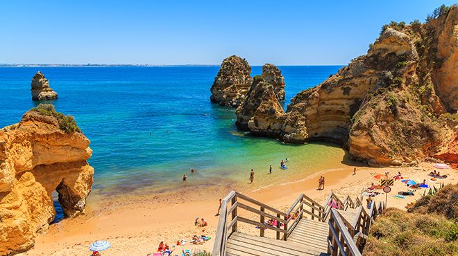 Praia dourada com rochas laranja e escadaria de madeira junto ao mar azul