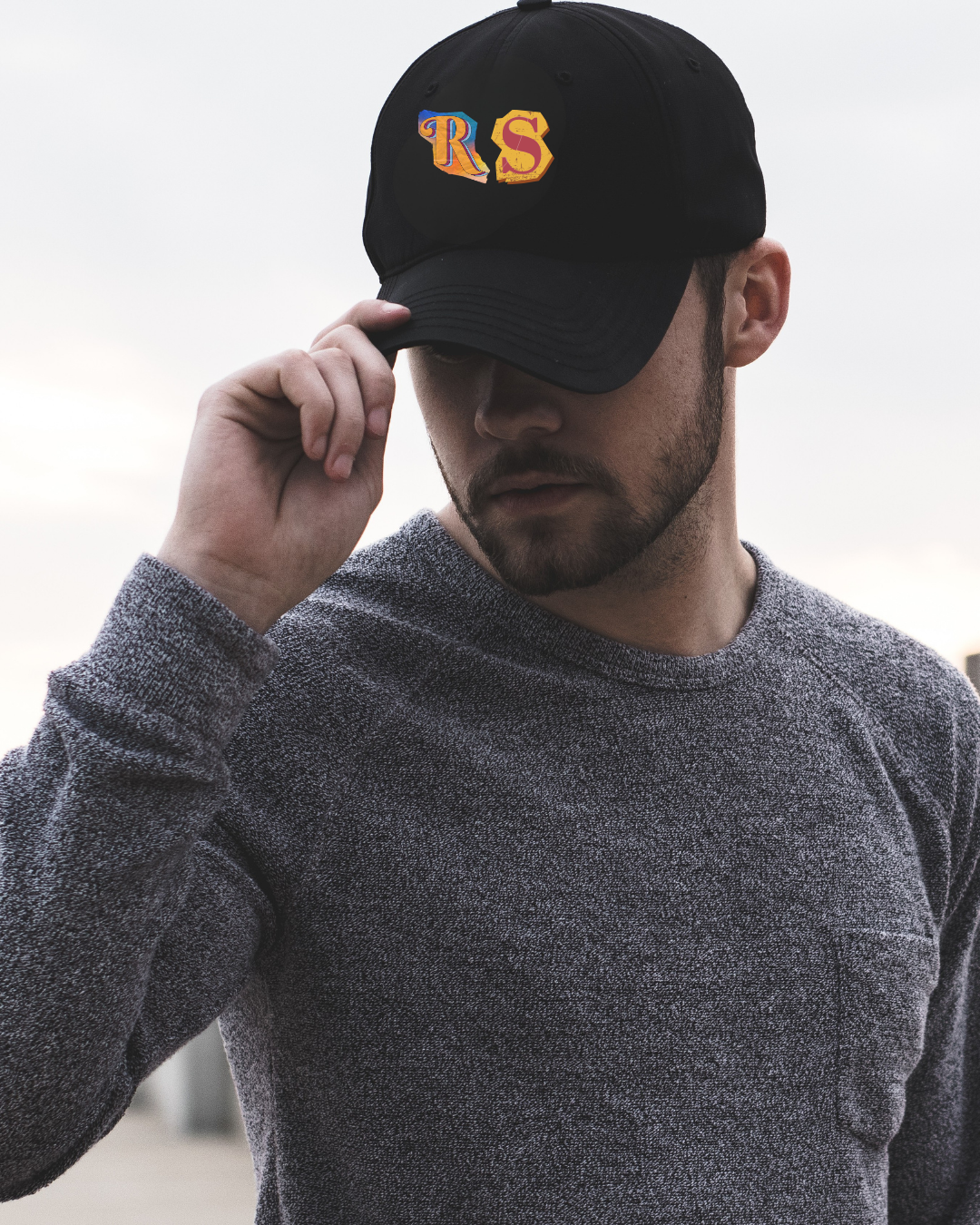 Homem com boné preto bordado com letras RS e camiseta cinzenta