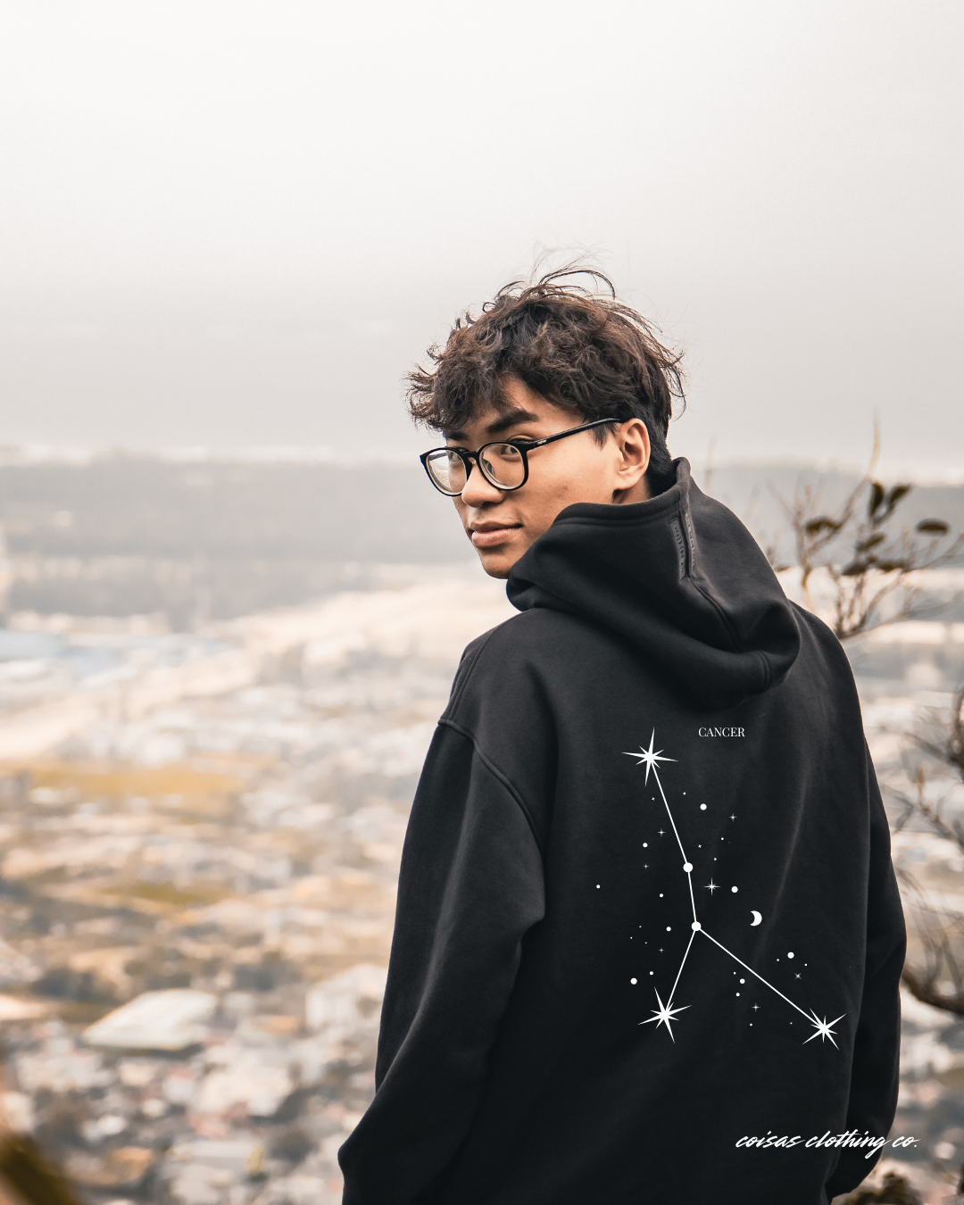 Casaco preto com estampa branca da constelação Cancer vista de costas num ambiente ao ar livre