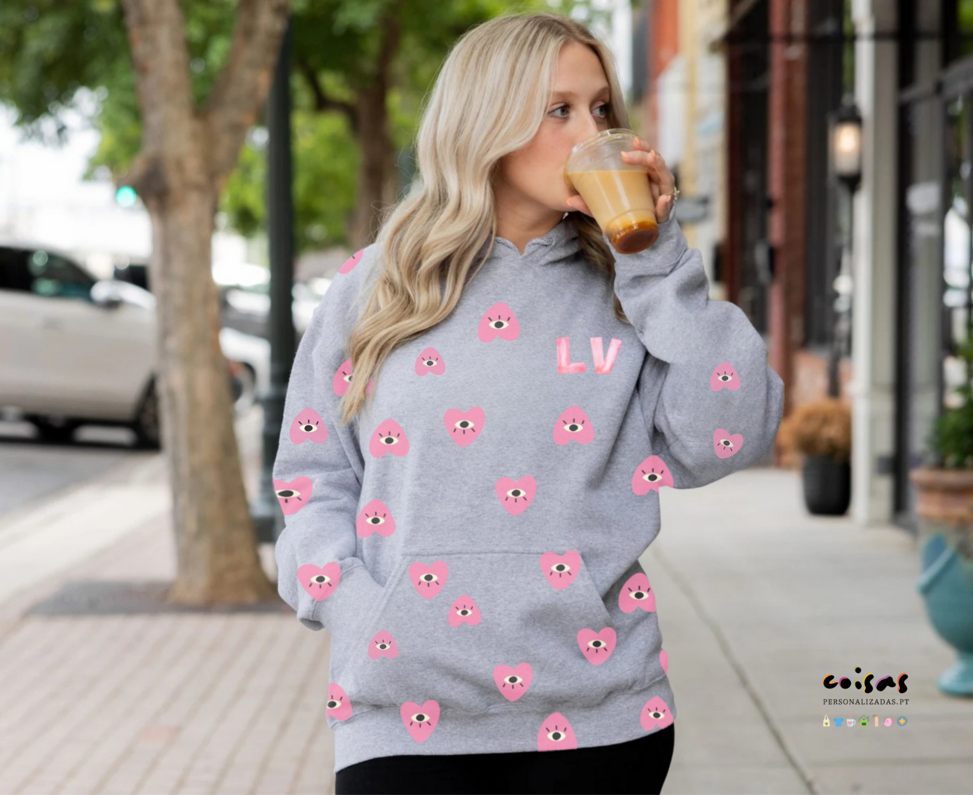 Mulher loira a usar casaco cinzento com corações rosa e letras LV a beber café na rua