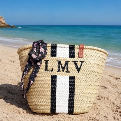 Bolsa de praia em palha trançada com listras e texto LMV na areia da praia