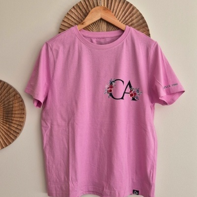 T-shirt rosa com logotipo e texto na manga pendurada num cabide