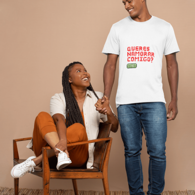 Homem com t-shirt branca com texto, mulher sentada em cadeira de madeira, fundo bege.