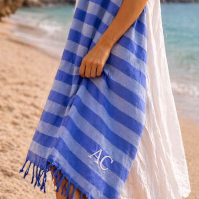 Toalha de praia azul com riscas e letras AC junto à praia.