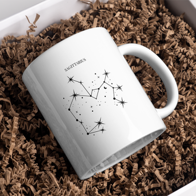 Caneca branca com constelação e texto S AGITTARIUS em caixa com papel castanho