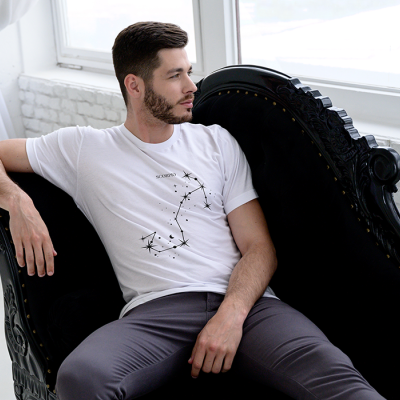 Homem sentado no sofá preto de veludo com t-shirt branca e calças cinzentas