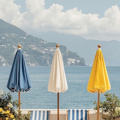 Três espreguiçadeiras às riscas azuis e brancas com três guarda-sóis fechados azul, branco e amarelo junto ao mar
