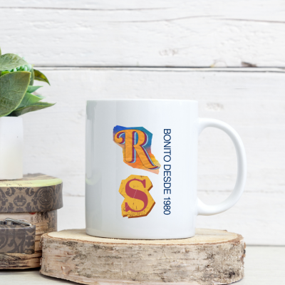 Caneca branca com letras coloridas R S e texto BONITO DESDE 1980 ao lado sobre base de madeira