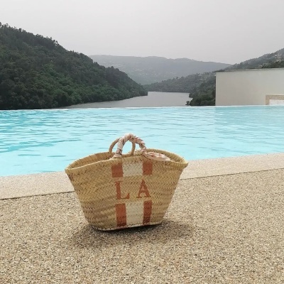 Porque as Cestas de Palha Pintadas à Mão estão novamente na Moda Cesto de palha com alças de corda junto a piscina com vista para colinas