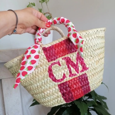 Cesto de palha trançada com alças de tecido estampado e letras CM vermelhas