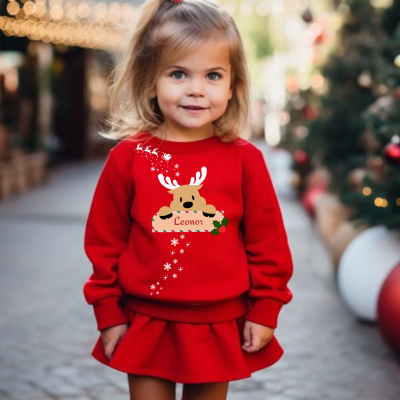 Menina pequena com vestido vermelho e camisola com rena personalizada Leonor, em ambiente natalício exterior