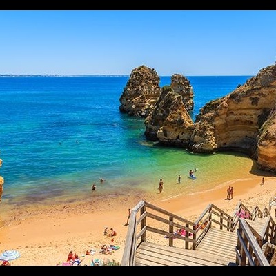Praia dourada com rochas laranja e escadaria de madeira junto ao mar azul