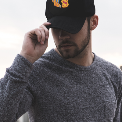 Homem com boné preto bordado com letras RS e camiseta cinzenta