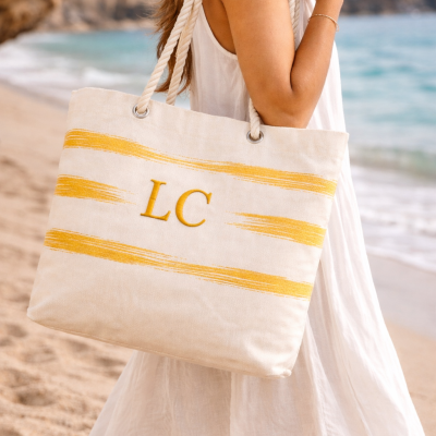 Sacola bege com listras amarelas e letras LC na praia