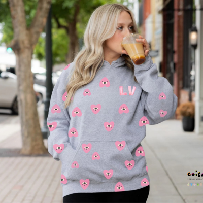 Mulher loira a usar casaco cinzento com corações rosa e letras LV a beber café na rua