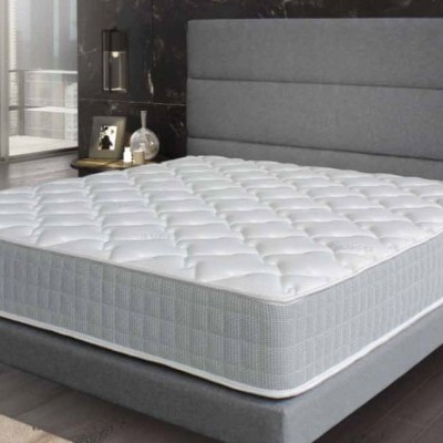 Colchão branco acolchoado em cama cinzenta com cabeceira acolchoada e mesa de cabeceira