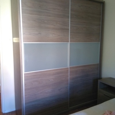 Armário de portas de correr em madeira castanha com faixas cinzentas no meio e moldura metálica