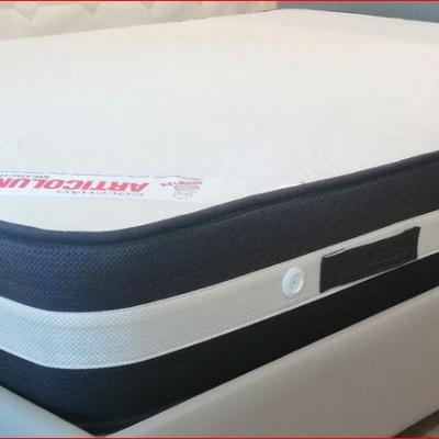 Colchão branco com laterais pretas e brancas sobre base de cama cinza