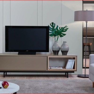 Móvel TV bege com decoração, televisão, lâmpada de pé, sofá e mesa branca redonda.