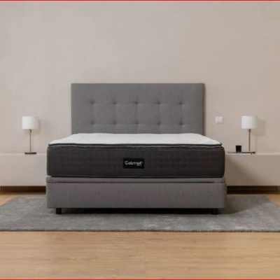 Cama cinza estofada com colchão cinza escuro e mobiliário branco em quarto minimalista