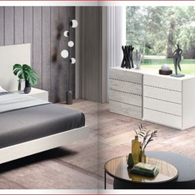 Quarto moderno com cama cinza e branco, mesas de cabeceira, cómoda branca e janela ampla.