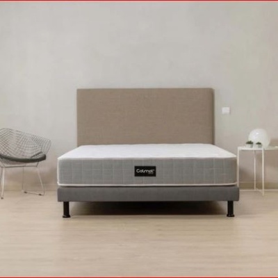 Cama com colchão cinza e cabeceira bege numa divisão minimalista.