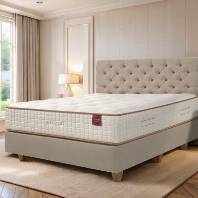 Cama de casal com colchão branco texturizado e cabeceira almofadada bege num quarto bem iluminado