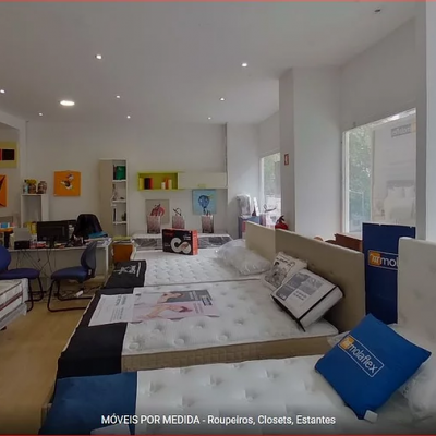 Loja de móveis com colchões brancos, almofadas azuis e chão de madeira clara