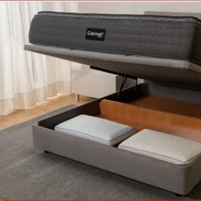 Cama cinzenta com colchão levantado e espaço de arrumação com almofadas duas almofadas