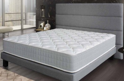 Colchão branco acolchoado em cama cinzenta com cabeceira acolchoada e mesa de cabeceira