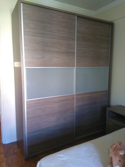 Armário de portas de correr em madeira castanha com faixas cinzentas no meio e moldura metálica