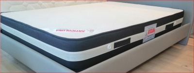 Colchão branco com laterais pretas e brancas sobre base de cama cinza