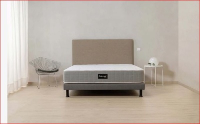 Cama com colchão cinza e cabeceira bege numa divisão minimalista.